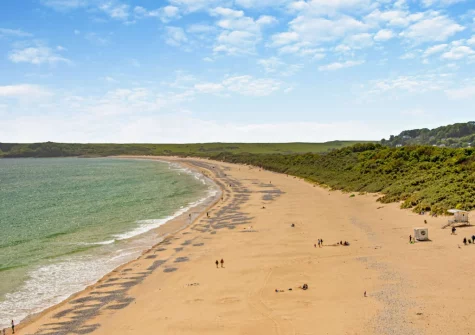 Visit Tenby South Beach, featuring a long sandy coastline with dunes & shallow waters