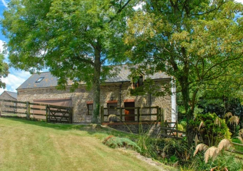 The farmhouse lawned garden, dotted with mature trees, at The Hayloft, Broad Haven