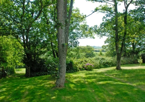 The farmhouse lawned garden, dotted with mature trees, at The Hayloft, Broad Haven